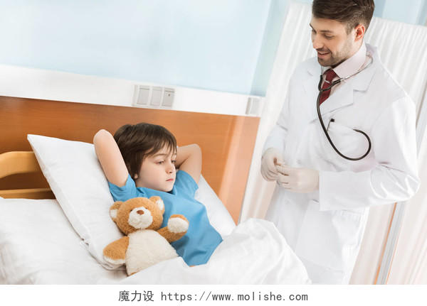 微笑着看着小男孩躺在医院床上的玩具熊的儿科医生儿科医生